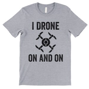 Op de afbeelding: Een grijs t-shirt met een zwarte afbeelding van een drone en de tekst "I Drone On And On".
