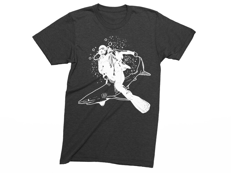 May include: Dark gray t-shirt featuring a white graphic of a scuba diver riding a shark. The diver is wearing a diving helmet, mask, and fins. Bubbles surround the diver and shark, creating a dynamic underwater scene.