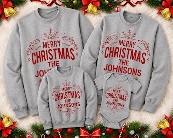 May include: A set of matching grey crewneck sweatshirts and a short-sleeve bodysuit featuring red text that reads Merry Christmas The Johnsons 2026, accented with red snowflake and holly leaf graphics printed on the front of each garment.