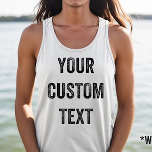 May include: White tank top with the text "YOUR CUSTOM TEXT" in black, with "*WHITE" at the bottom. The tank top has a racerback design and is made of a soft material. The background is a blurred view of water.
