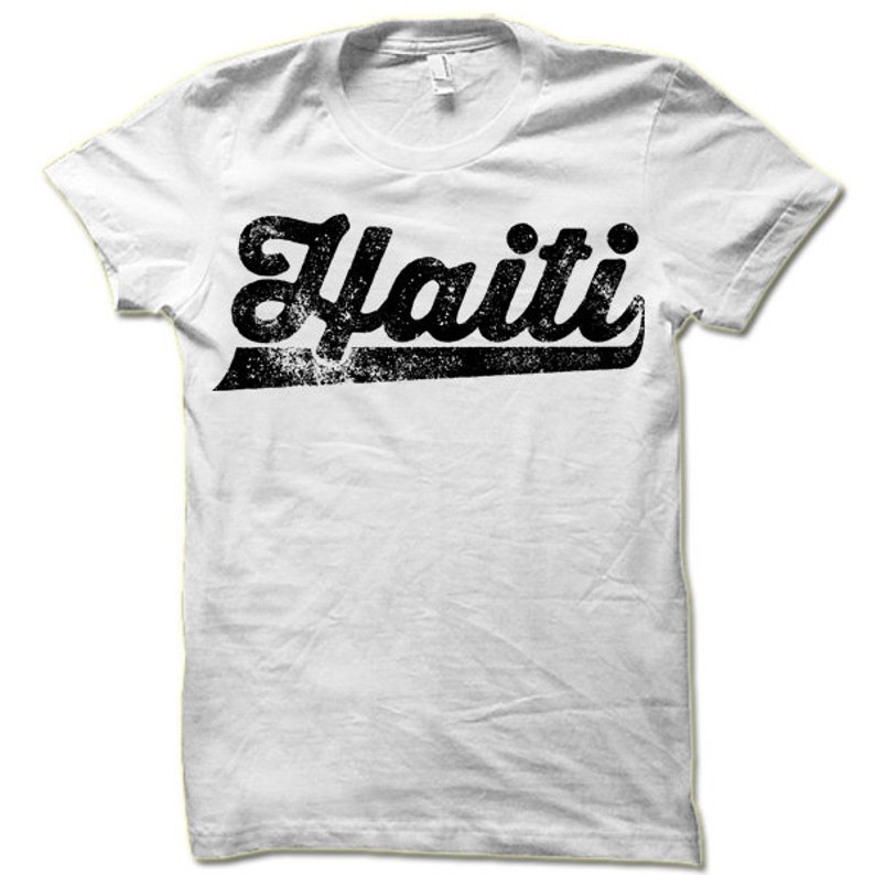 May include: White t-shirt with a black vintage-style graphic that says "Haiti" in a bold, cursive font.