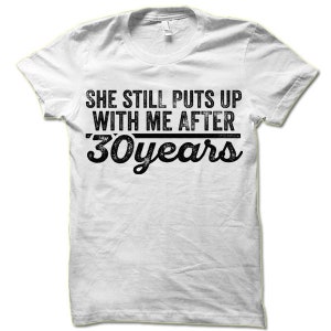 May include: White t-shirt with black text that reads "She still puts up with me after 30 years".