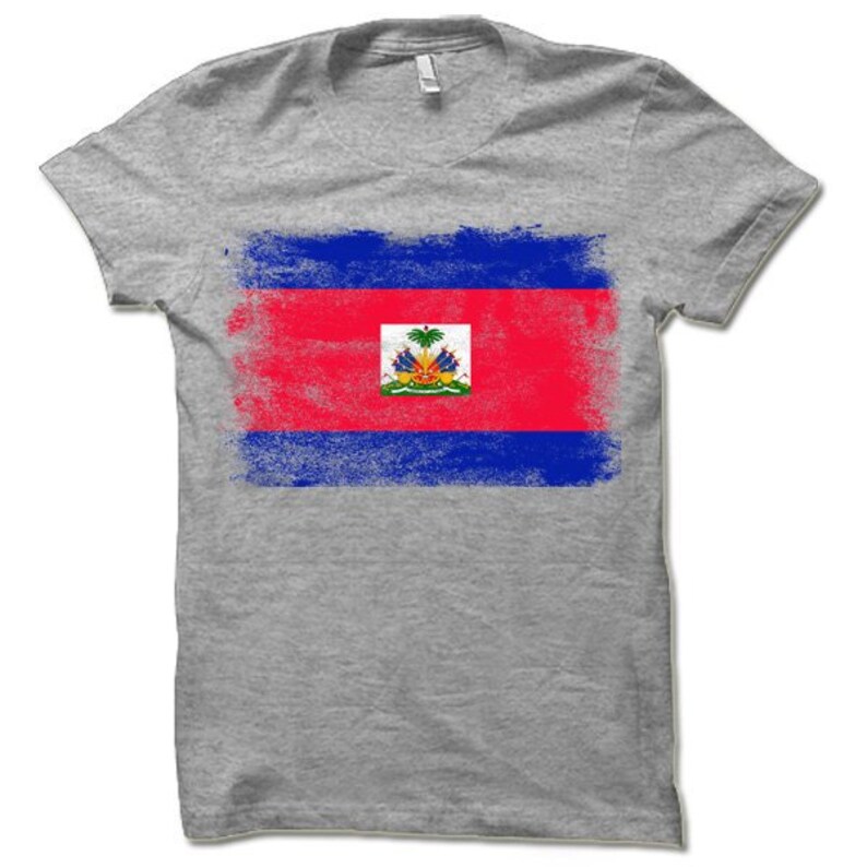 May include: A gray t-shirt with a distressed, faded design of the Haitian flag. The flag features the colors blue, red, and white, with the coat of arms in the center.