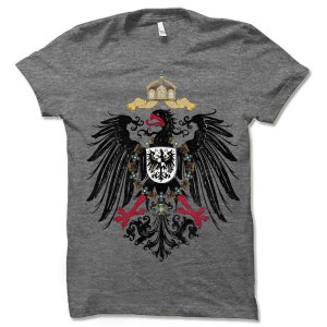 May include: A heather grey t-shirt with a black and white image of the German Imperial Eagle. The eagle is holding a shield with a black eagle on a white background. The eagle is surrounded by a wreath of gold and blue.