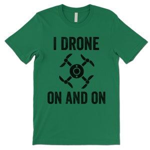 Op de afbeelding: Groen T-shirt met zwarte tekst die "I Drone On And On" luidt en een zwart silhouet van een drone.