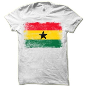 May include: White t-shirt with a distressed, faded print of the flag of Ghana. The flag is red, yellow, green, and black with a black star in the center.