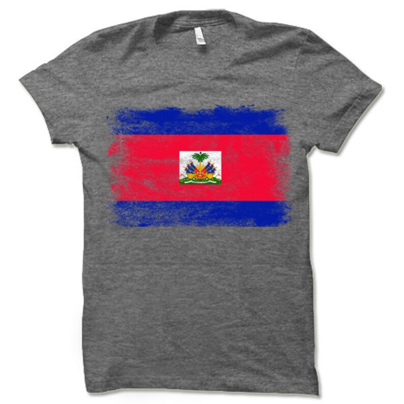May include: A heather grey t-shirt with a distressed, faded design of the Haitian flag. The flag features a red, blue, and blue horizontal stripe pattern with the Haitian coat of arms in the center.