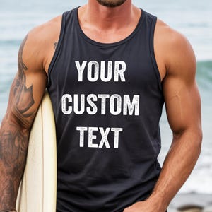 May include: Black tank top with the text "YOUR CUSTOM TEXT" in white. The tank top is sleeveless and has a round neckline. The person is holding a surfboard.
