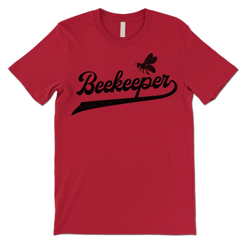 Puede incluir: Camiseta roja de manga corta con un gr&aacute;fico de abeja negra y el texto "Beekeeper" en una fuente de estilo vintage de camiseta de b&eacute;isbol.