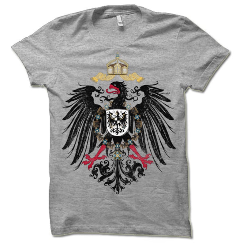 May include: A grey t-shirt with a black and red eagle design. The eagle is holding a shield with a black eagle on it. The eagle is surrounded by a crown and a floral design.