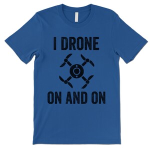 Op de afbeelding: Een koninklijk blauw t-shirt met een zwarte afbeelding van een drone en de tekst "I Drone On And On".