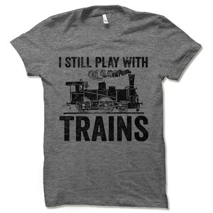 May include: A heather grey t-shirt with a vintage-style graphic of a train and the text "I still play with trains".