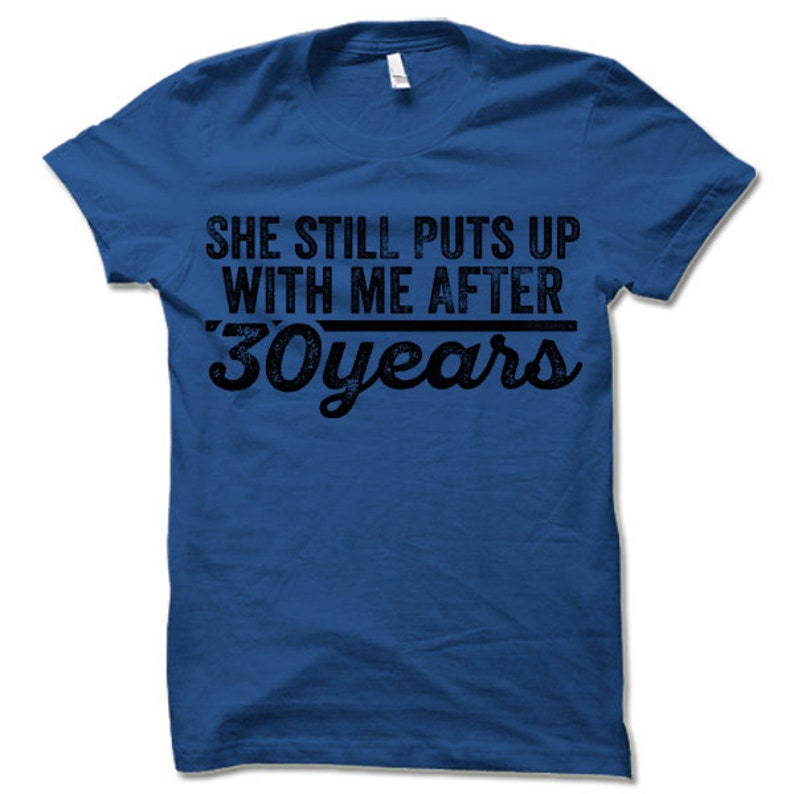 May include: A royal blue t-shirt with a distressed black graphic that reads "She still puts up with me after 30 years".