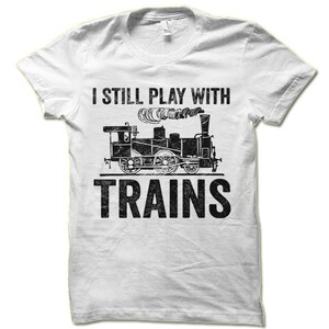 May include: White t-shirt with a black graphic of a train and the text "I still play with trains".