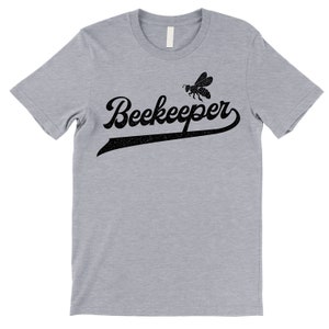 Puede incluir: Una camiseta gris jaspeada con un gr&aacute;fico negro de una abeja y el texto "Beekeeper" en una fuente de b&eacute;isbol vintage.