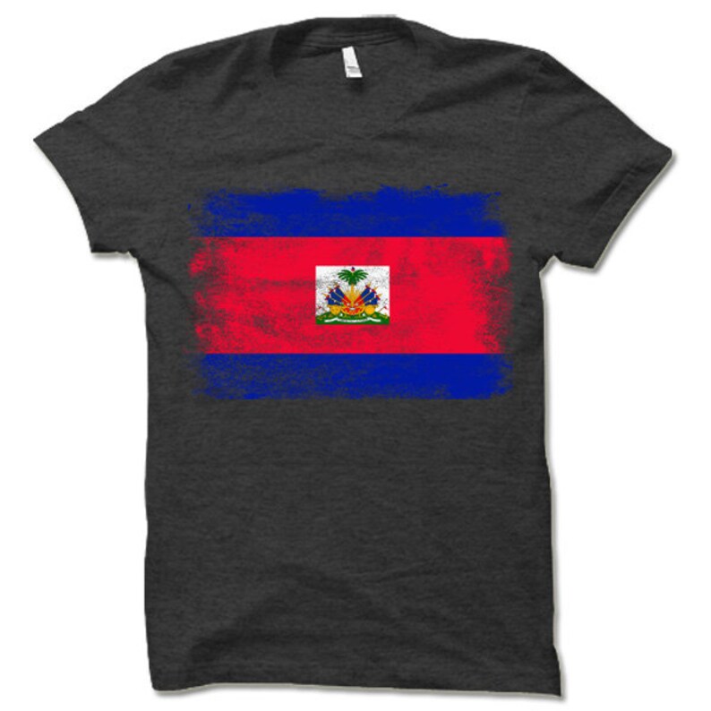 May include: A dark grey t-shirt with a distressed, faded design of the Haitian flag. The flag features the colors red, blue, and white, with a coat of arms in the center.