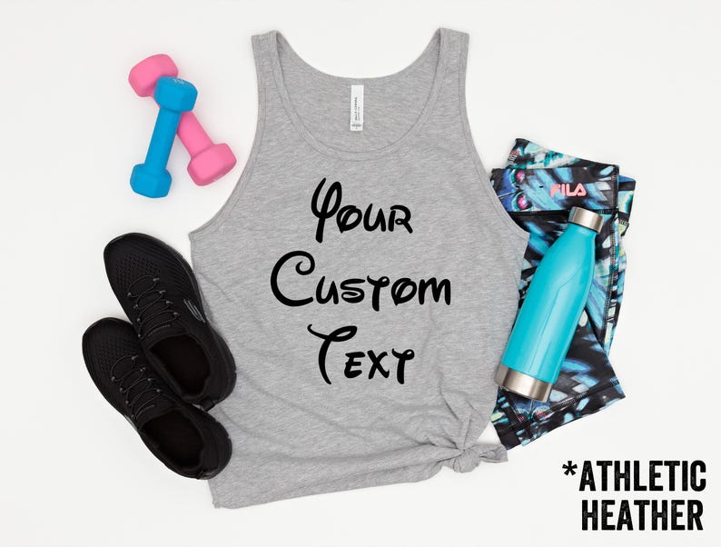 May include: A gray athletic heather tank top with the text "Your Custom Text" in black script. The image also includes black sneakers, pink and blue dumbbells, a teal water bottle, and patterned leggings.