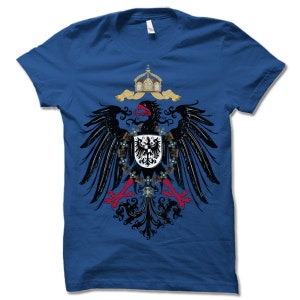 May include: A royal blue t-shirt with a black eagle graphic. The eagle is holding a shield with a black cross on a white background. The eagle is surrounded by a crown and a scroll.
