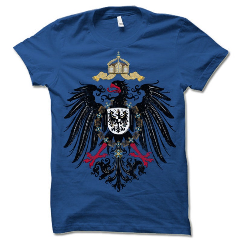 May include: A royal blue t-shirt with a black eagle graphic. The eagle is holding a shield with a black cross on a white background. The eagle is surrounded by a crown and a scroll.