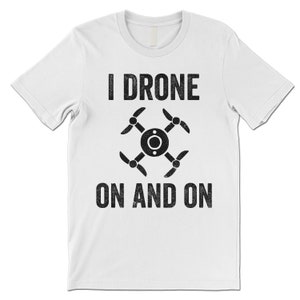 Op de afbeelding: Wit T-shirt met zwarte tekst die "I Drone On And On" zegt en een zwart silhouet van een drone.