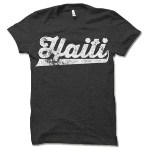 May include: A dark gray t-shirt with a white vintage-style graphic that says "Haiti" in a bold font.