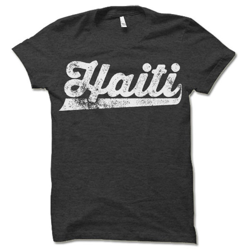 May include: A dark gray t-shirt with a white vintage-style graphic that says "Haiti" in a bold font.