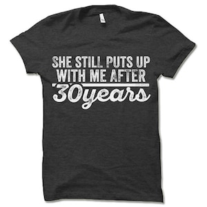 May include: Dark gray t-shirt with white text that reads "She still puts up with me after 30 years".
