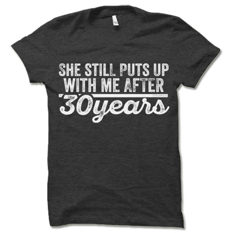 May include: Dark gray t-shirt with white text that reads "She still puts up with me after 30 years".
