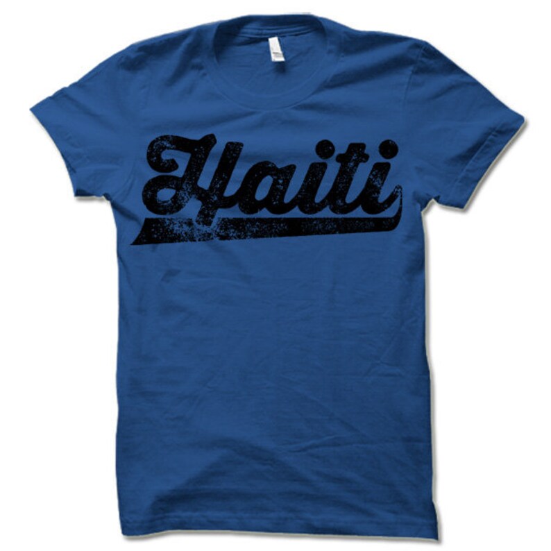 May include: A royal blue t-shirt with a black distressed graphic of the word "Haiti" in a retro font.