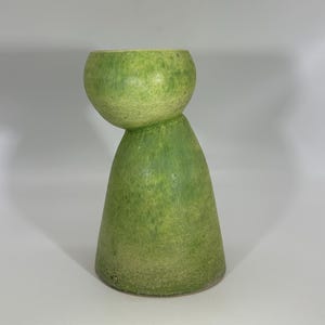May include: A green ceramic vase with a unique, rounded top and a conical base. The vase has a textured surface and a light green color with darker green accents. The design is modern and artistic, suitable for home decor.