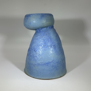 Op de afbeelding: Een handgemaakte keramische vaas in blauwtinten. De vaas heeft een afgeronde bovenkant en een getextureerde, conische body. De kleur gaat over van een lichter blauw aan de bovenkant naar een dieper blauw aan de basis. De vaas is een uniek kunstwerk.