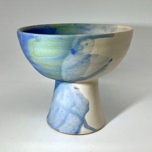 May include: A white ceramic bowl with a blue and green glaze. The bowl is on a pedestal.