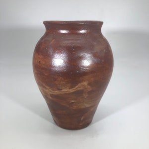 May include: A brown ceramic vase with a rounded body and a slightly flared opening. The vase has a mottled brown glaze with subtle variations in color.