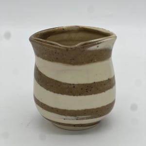 May include: A small, white and brown striped ceramic pitcher with a rounded base.
