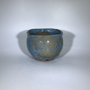 May include: A small, square, blue and brown ceramic planter with a textured glaze. The planter has a slightly rounded bottom and a wide, open top.