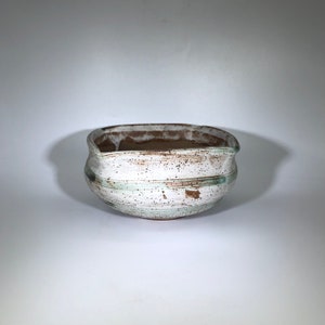 May include: A white ceramic bowl with brown and green glaze. The bowl has a rounded shape and a slightly flared rim.