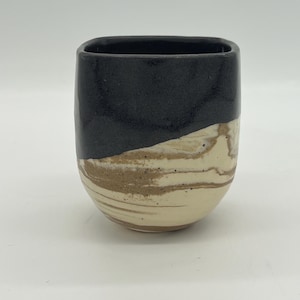 May include: A ceramic cup with a black top and a white and brown marbled bottom.