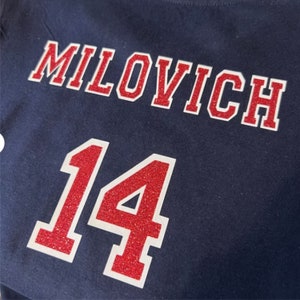 May include: A navy blue t-shirt with the name "MILOVICH" and the number "14" in red glitter with white outlines.