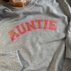May include: Gray sweatshirt with the word "AUNTIE" in gold glitter letters outlined in pink.