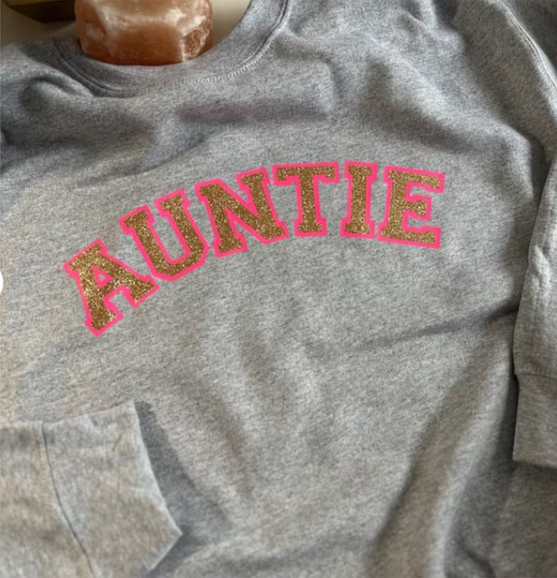 May include: Gray sweatshirt with the word "AUNTIE" in gold glitter letters outlined in pink.