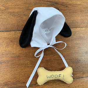 May include: White felt dog costume hood with black felt ears and a white ribbon. A yellow felt bone with the word "WOOF!" embroidered on it is included.