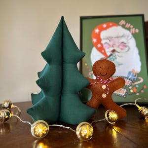 Könnte beinhalten: Ein grüner Filz-Weihnachtsbaum mit einem Lebkuchenmann-Anhänger. Der Baum ist mit einer Lichterkette mit kleinen goldenen Glöckchen geschmückt.