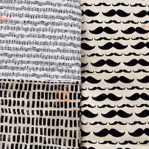 May include: A fabric display with three patterns. One shows black musical notes on white with the word "Music". Another features black moustaches on beige with the word "Moustache". The third has a black and white abstract design with the words "Brush Strokes".