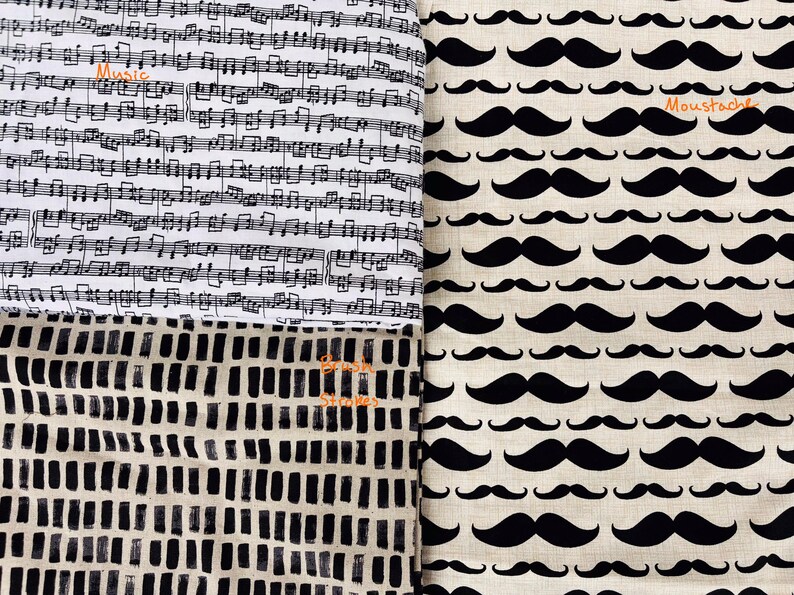 May include: A fabric display with three patterns. One shows black musical notes on white with the word "Music". Another features black moustaches on beige with the word "Moustache". The third has a black and white abstract design with the words "Brush Strokes".