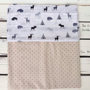 May include: Folded fabric with two distinct patterns. The top section features a white background with a wood grain design, adorned with black silhouettes of deer, moose, bears, and teepees. The bottom section displays a tan polka dot pattern.