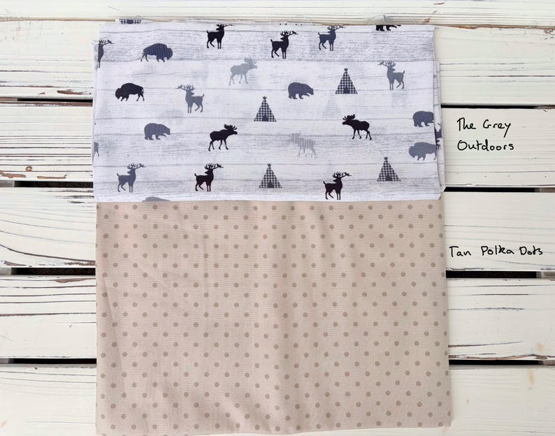 May include: Folded fabric with two distinct patterns. The top section features a white background with a wood grain design, adorned with black silhouettes of deer, moose, bears, and teepees. The bottom section displays a tan polka dot pattern.