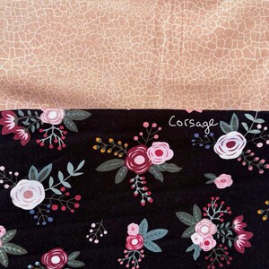 May include: A fabric sample with two contrasting designs. The top section has a tan, cracked pattern with the word "Desert". The bottom section features a black floral design with pink and white roses, green leaves, and the word "Corsage".