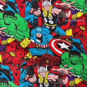 May include: A colourful fabric print showcasing various comic book superheroes. The design includes Captain America, Thor, Spider-Man, and the Hulk, with the word "Superheroes" visible. The characters are in their classic costumes, with bold colours and dynamic poses.