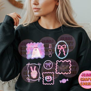 May include: Black sweatshirt with a colorful Halloween-themed graphic. The design includes a ghost, bows, a peace sign, a jack-o'-lantern, and candy. The text "BOO" is also visible. The sweatshirt has the text "JENNS CRAFTY CORNER".
