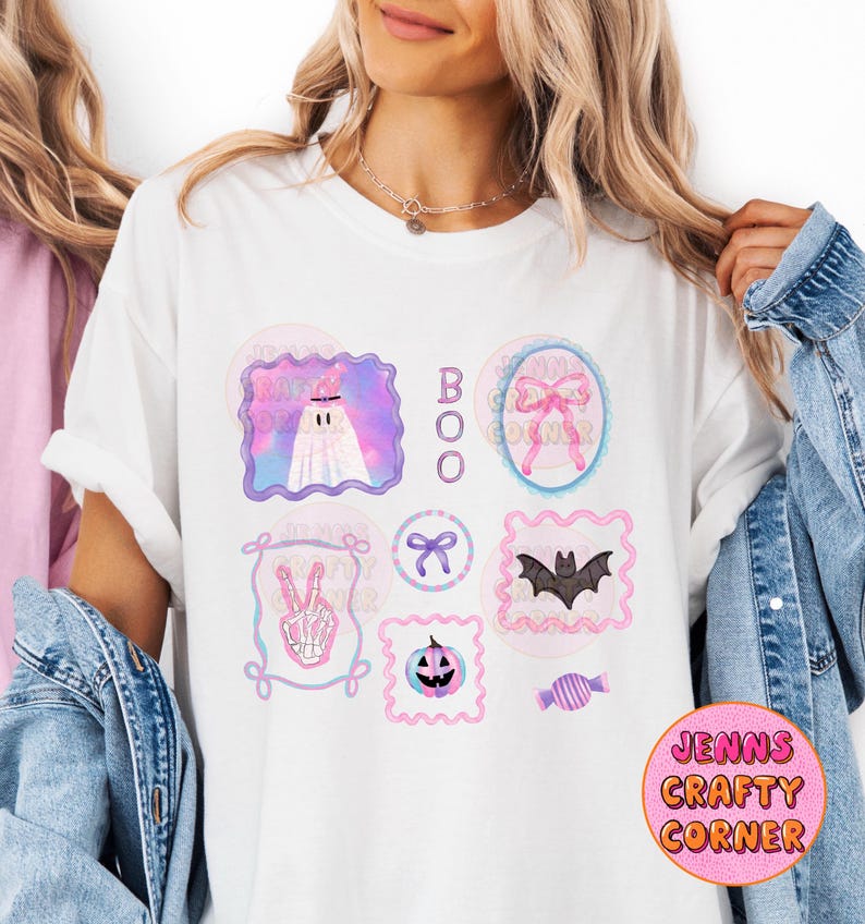May include: White t-shirt with a colorful Halloween-themed design. The design includes a ghost, a bat, a jack-o'-lantern, and the word "BOO". The shirt also features the text "Jenns Crafty Corner" in a pink circle.